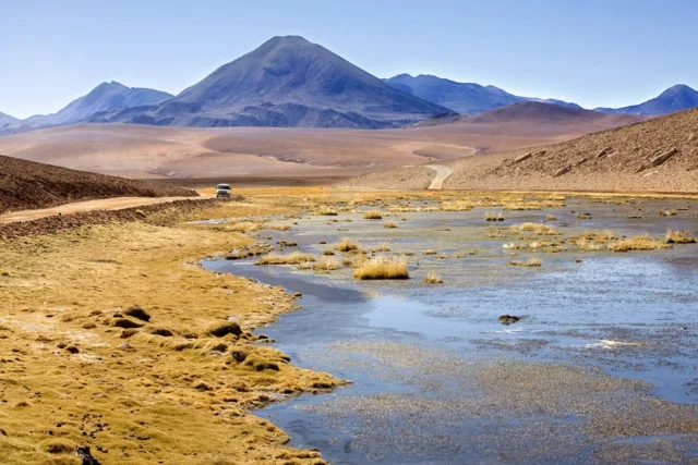 Imagen de Rio Grande en el desierto Chileno de Atacama con unas montañas de fondo y un vehículo todoterreno circulando por un camino