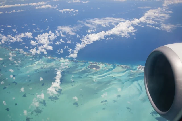 Imagen aérea de Islas Bahamas marcada por unos intensos tonos azules y turquesas del océano y sus arrecifes con un salpicado de pequeñas nubes que proyectan sus sombras sobre el agua