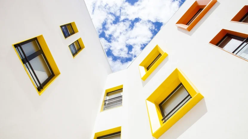 Imagen de la fachada de un edificio de viviendas con varias ventanas de diferentes tamaños y formas con los marcos pintados de diferentes colores
