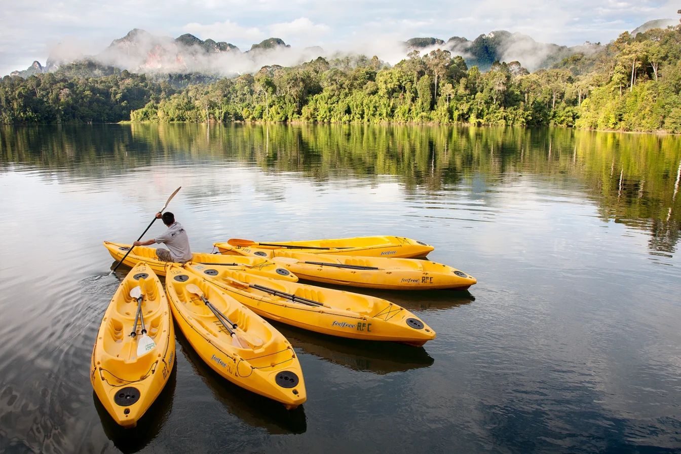Imagen de un lago en la que se puede observar como un operario maneja varias canoas amarillas para turistas y al fondo una intensa vegetación compuesta de grandes árboles